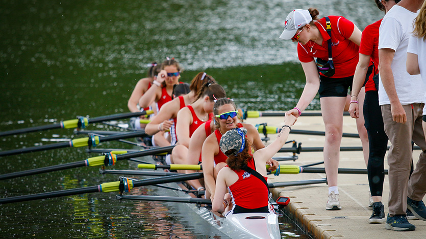 Image of Carina Pascucci ’26 in the stern of the boat receiving encouragement from Assistant Rowing Coach Marguerite McGahay ’25.