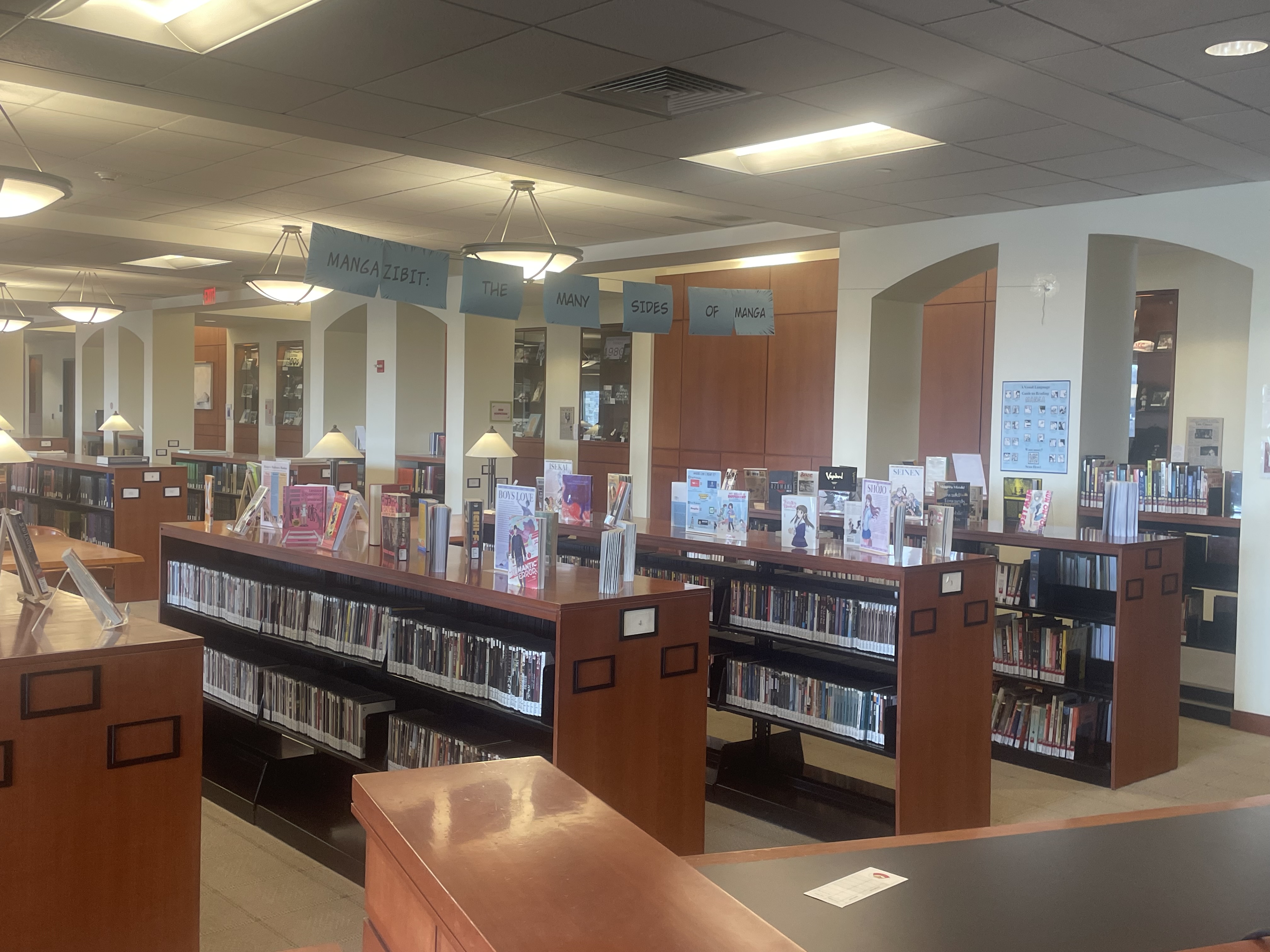 A library display featuring numerous manga books underneath a big banner reading "Mangazibit: The Many Sides of Manga" display.